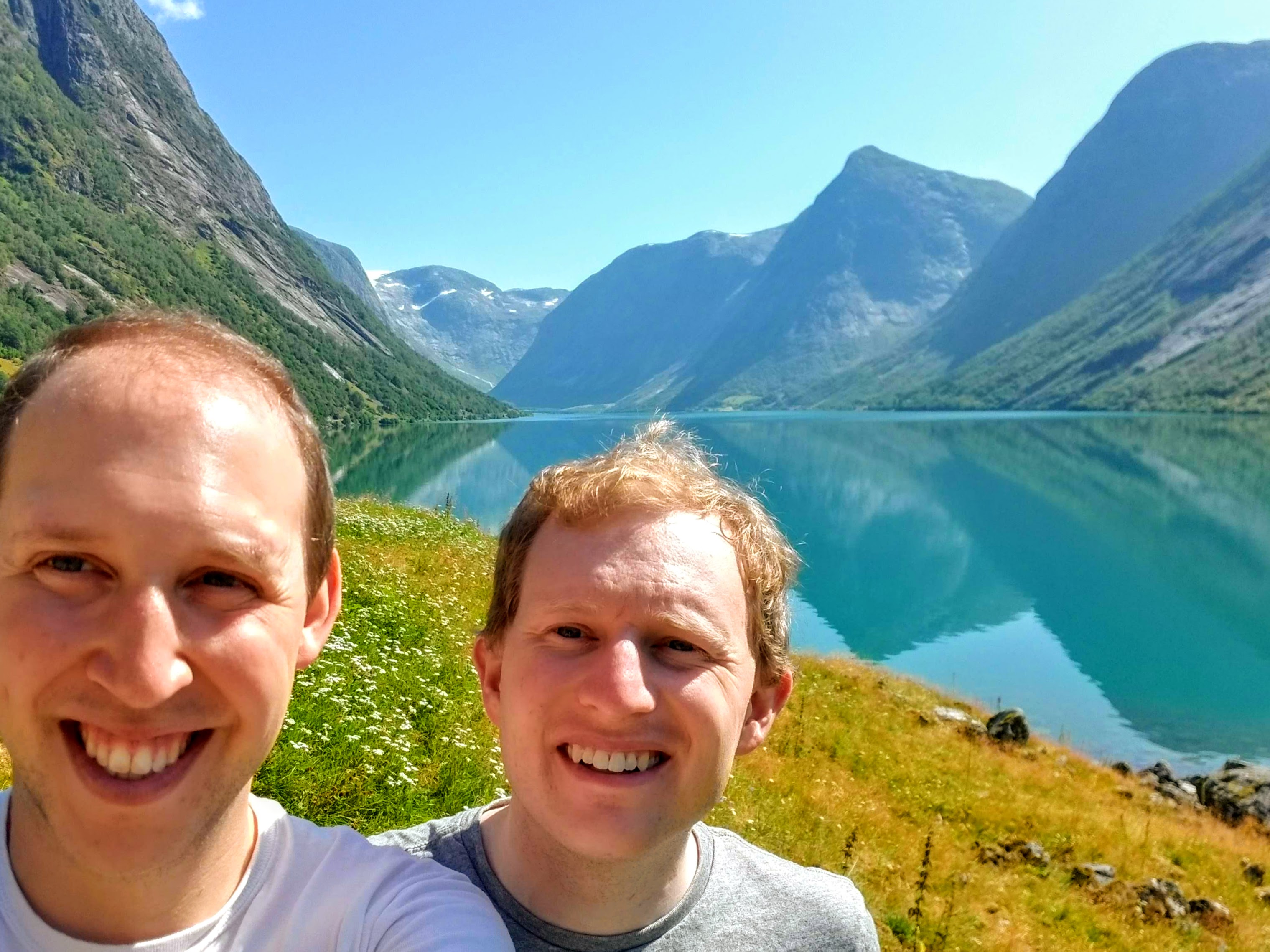 A selfie of two men in front of a blue lake and mountains in Norway.